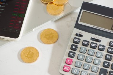 Altın bir fiziksel Bitcoin bir smartphone ekran, sikke yığını ve beyaz arka plan üzerinde bir hesap makinesi