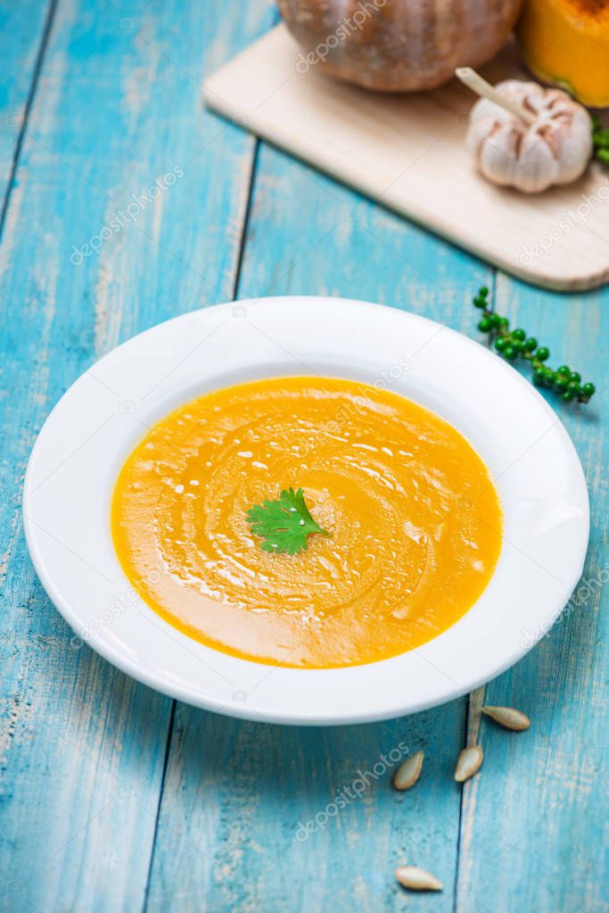 Pumpkin and carrot soup with cream and parsley on blue wooden background.
