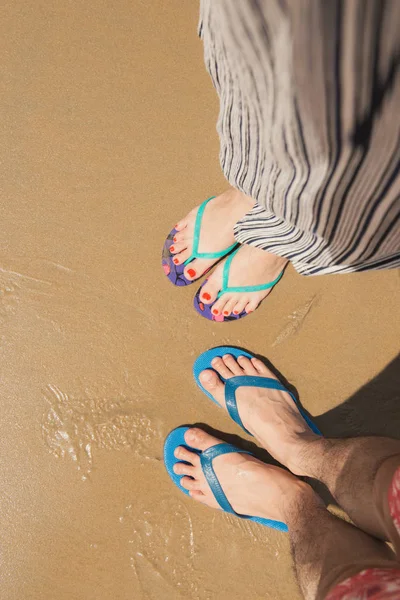 Couple feet in sandals on beach sand background
