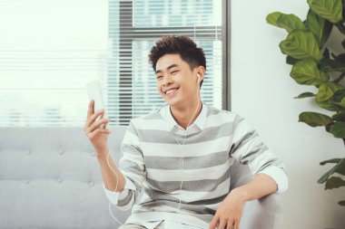 Müzik dinlerken rahat kanepe üzerinde oturan gülümseyen Asya yakışıklı adam