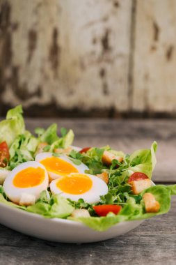 Yüksek açılı görünüş ile haşlanmış yumurta dilimleri, besleyici sebze salatası hizmet bir ahşap masa üstünde beyaz bir plaka üzerinde