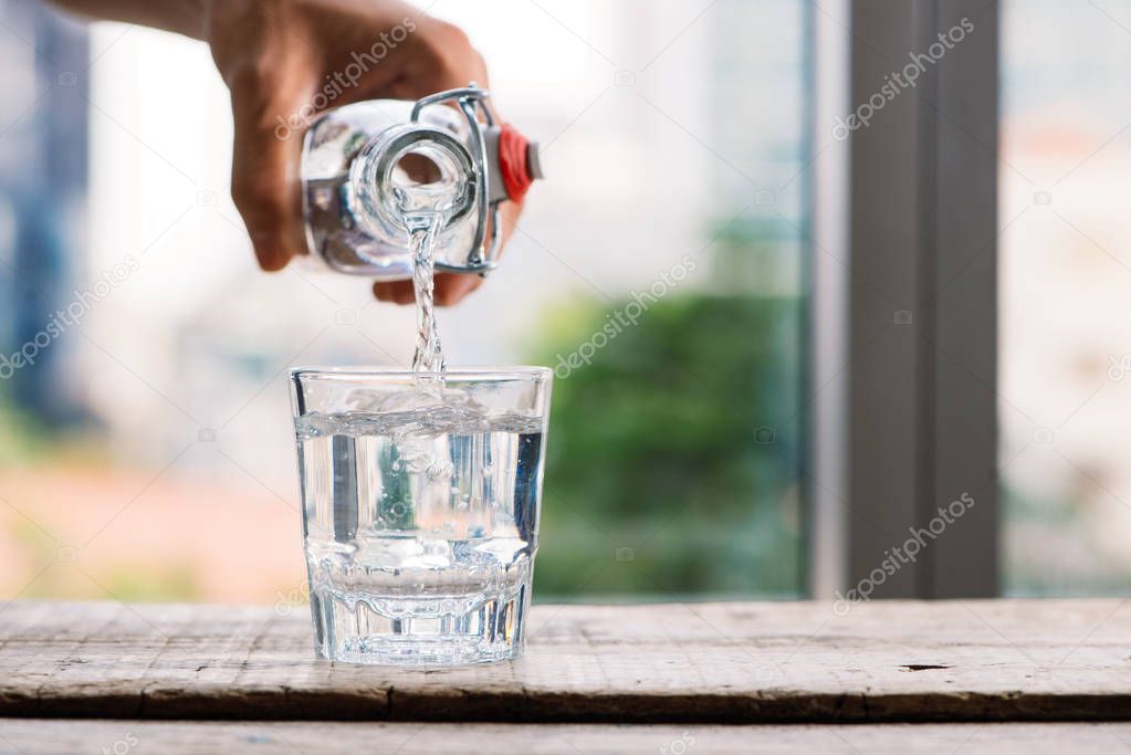 Pouring purified fresh drink water from bottle into glass on table