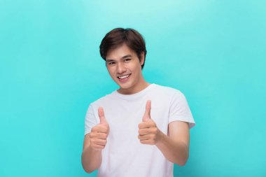 Portrait of a happy young man showing thumbs up gesture standing over gray wall clipart