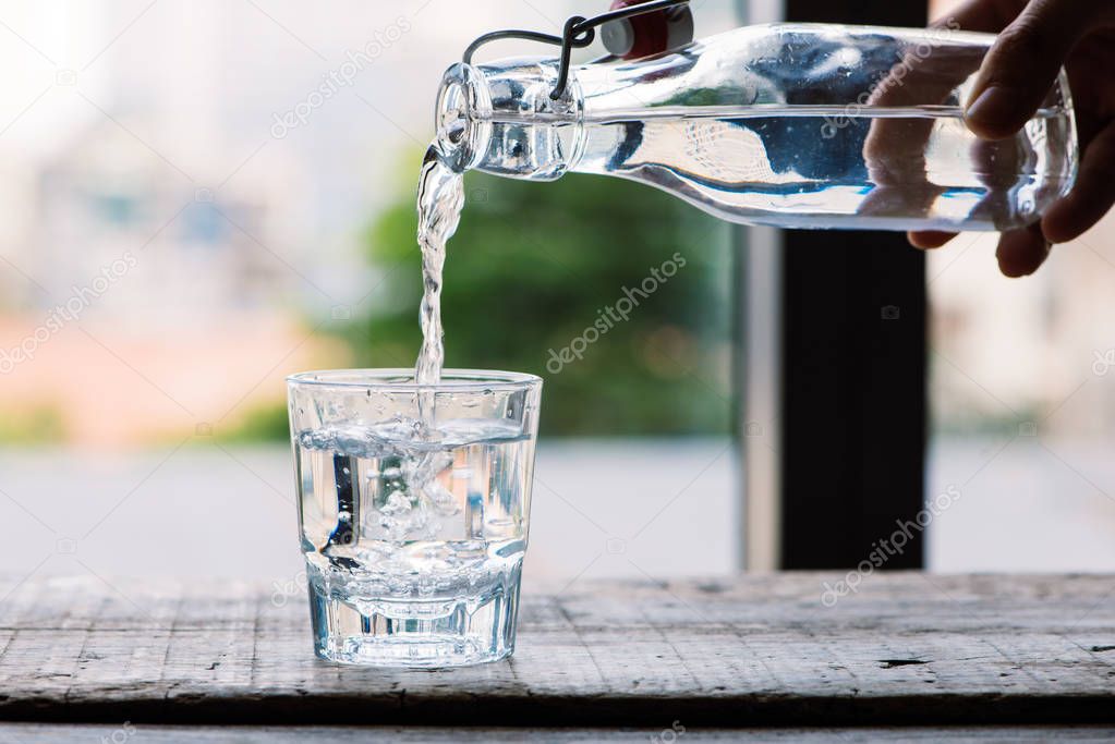 Pouring purified fresh drink water from bottle into glass on table