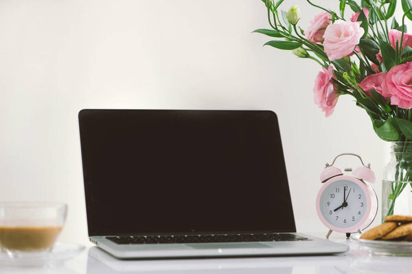 8 am clock. Cookies and flowers on the office desk with laptop showing screen.