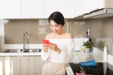Genç bir kadın mutfakta akıllı telefon kullanıyor..