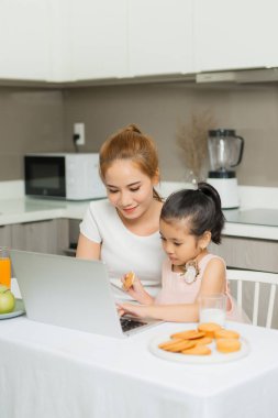Kızı olan genç bir ebeveyn masada oturuyor ve dizüstü bilgisayardan bir şeyler izliyor..
