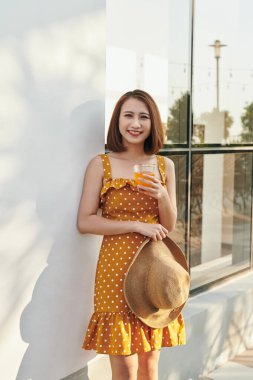 Vintage elbise giyen ve duvar arkasında portakal suyu ile şapka tutan Pretty Asya kız