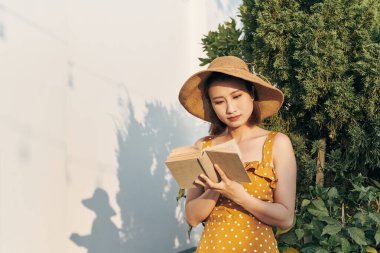 Genç kadın yalın gövde ağacına yaz Park açık duran bir kitap okuma.