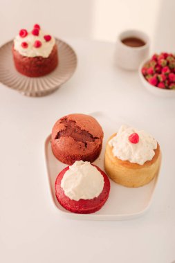 Ahududu ve kahve fincan bir kase ile beyaz tabakta çeşitli kekler