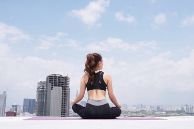 Hareketli genç sporcu kadın yoga eğitimi sırasında çatıda otururken poz veriyor.