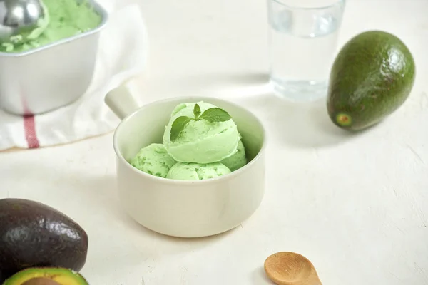 Avocado ice cream balls on a white plate, a spoon on a white background.