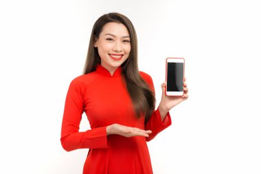 Aao dai elbisesi içindeki çekici kadın ekranda cep telefonunu gösteriyor, beyaz arka planda izole edilmiş.