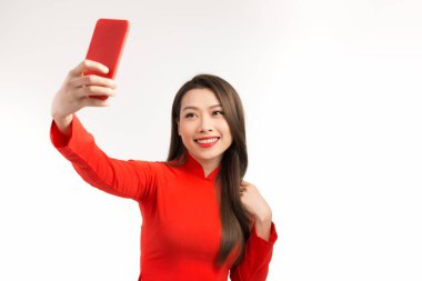 Vietnamlı Asyalı kadın geleneksel ao dai elbisesi giyiyor. Güzel, dişlek, gülümseyen genç bir kadın. Akıllı telefon kullanıyor. Arkadaşlarıyla görüntülü konuşma yapıyor..