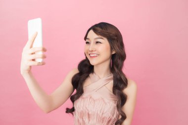 pembe elbise giymiş güzel bir genç asyalı kadın ayakta ve selfie çekerken poz
