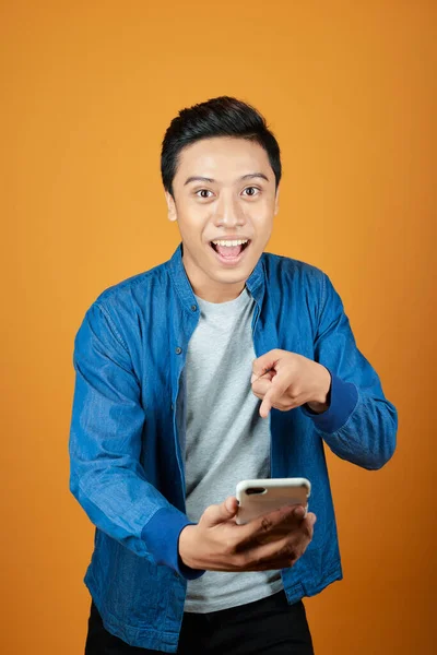 若いアジアの男性は 彼がスマートフォンを見て驚いた オレンジ色の背景に — ストック写真