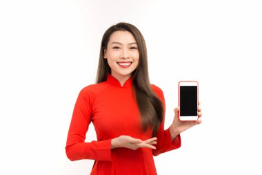 Kırmızı Ao Dai giyen ve telefonunu gösteren güzel bir kadın. Beyaz arkaplan üzerinde izole edilmiş.