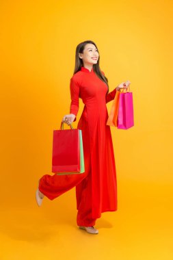 Güzel Asyalı kız sarı arka planda Ao Dai Vietnam giyerken elinde renkli alışveriş çantaları tutuyor..