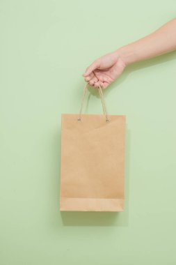 Yeşil arka planda kağıt alışveriş torbası tutan kadın.
