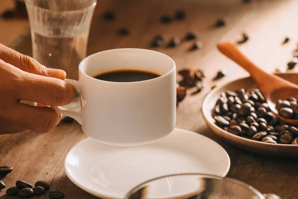 A cup of coffee with water, coffee beans and tea on wooden background