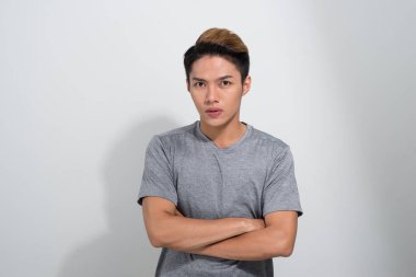 Genç Asyalı erkek kameraya bakıyor. Ellerini beyaz arka planda çapraz yapmış..
