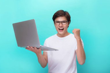 Bir laptop ve başarı bir yumruk gösteren bir mutlu heyecanlı genç Asya adam