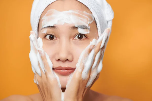 Mooi Aziatisch Meisje Doet Crème Haar Gezicht Geïsoleerd Oranje Achtergrond — Stockfoto