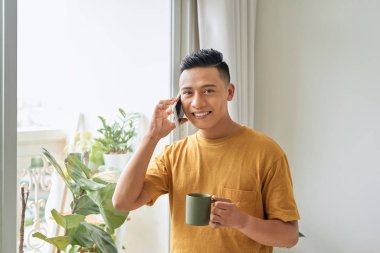 Sabah ları cep telefonuyla pencereden konuşan gündelik kıyafetler giyen genç adam