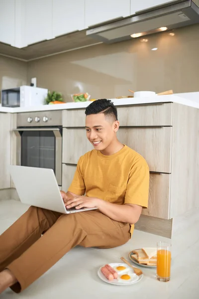 Atencioso Asiático Homem Usando Laptop Enquanto Sentado Chão Cozinha — Fotografia de Stock