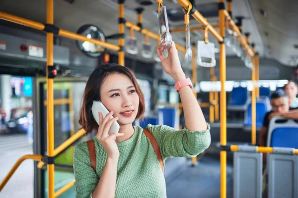 Asian woman standing in city bus and talking on mobile phone.