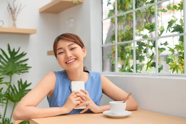 Happy Young Asian Woman Smiling While Using Phone Drinking Coffee — ストック写真