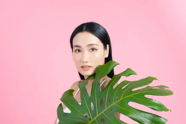 Portrait of young beautiful Asian woman holding tropical leaf on