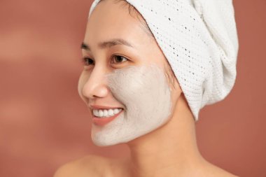 Yüzünde kil kozmetik maske olan mutlu ve pozitif, çıplak bir kadının duygusal portresi.