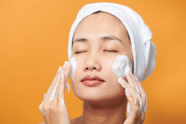 Beautiful Asian girl putting cream on her face. isolated on orange background.