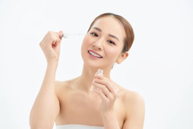 Yakın plan genç Asyalı kadın yüzüne serum uyguluyor. Temiz yumuşak makyaj ve izole edilmiş beyaz arkaplan.