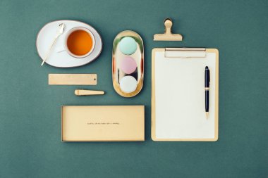 Düz yerde kadınsı bir iş yeri vardı. Yeşil arka planda defter, kalem, badem kurabiyesi ve yeşil çay..