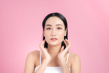 Güzel Asyalı Kız yüzüne dokunuyor ve gülümsüyor, tenini şımartıyor. Pembe arkaplan