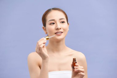 Genç bir kadının portresi menekşe arka planda yüzüne serum uyguluyor.