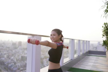 Kararlı bir kadın sabah dambıllarıyla dışarıda egzersiz yapıyor..