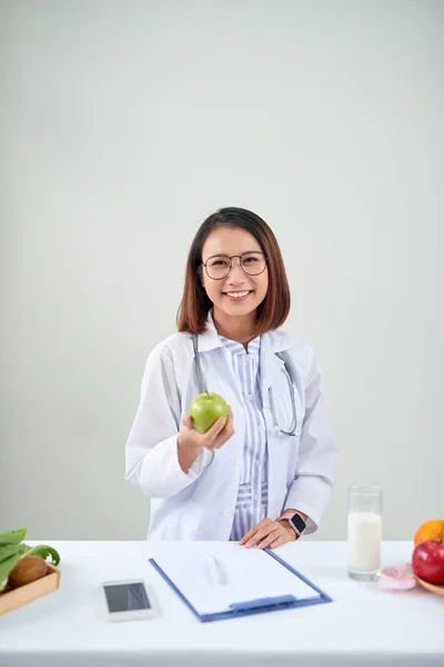 Smiling nutritionist in her office, she is showing healthy vegetables and fruits, healthcare and diet concept.