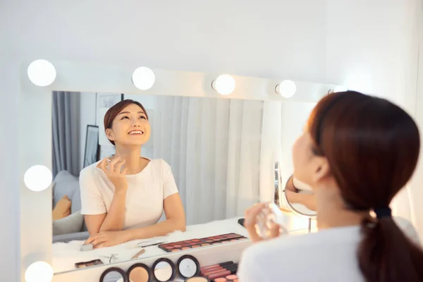 Cheerful Asian woman applying perfume in front of mirror