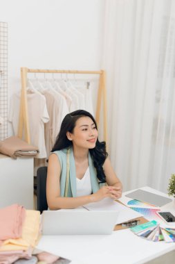 Genç Asyalı moda tasarımcısının portresi atölyede dizüstü bilgisayarının önünde oturuyor.