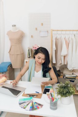 Moda tasarımcısı iş başında. Mutlu genç Asyalı kadın moda atölyesinde onu iş yerinde otururken çizim