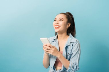 Asyalı kadın 20s cep telefonu tutarak ve mavi arka plan üzerinde gülümseyen