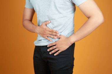 Turuncu arka planda duran genç adam mide acısından muzdarip.