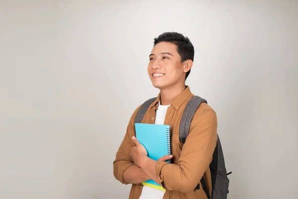 Portrait of smiling young college Asian student with books and backpack against white background