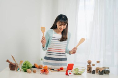 Güzel genç asyalı kadın yemek tarifi okuma veya salata yaparken göstermek izlerken