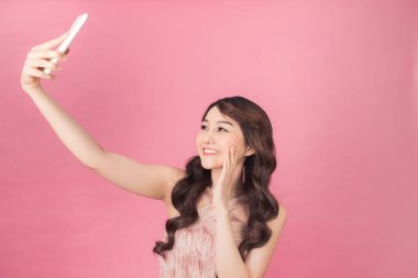 pembe elbise giymiş güzel bir genç asyalı kadın ayakta ve selfie çekerken poz