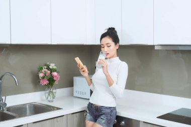 Genç Asyalı mutfakta süt içerken telefon kullanıyor..