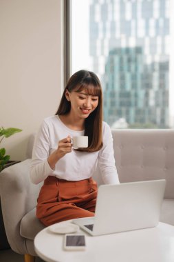 Kız sabah kahveiçme ve kanepede oturarak dizüstü bilgisayar kullanarak